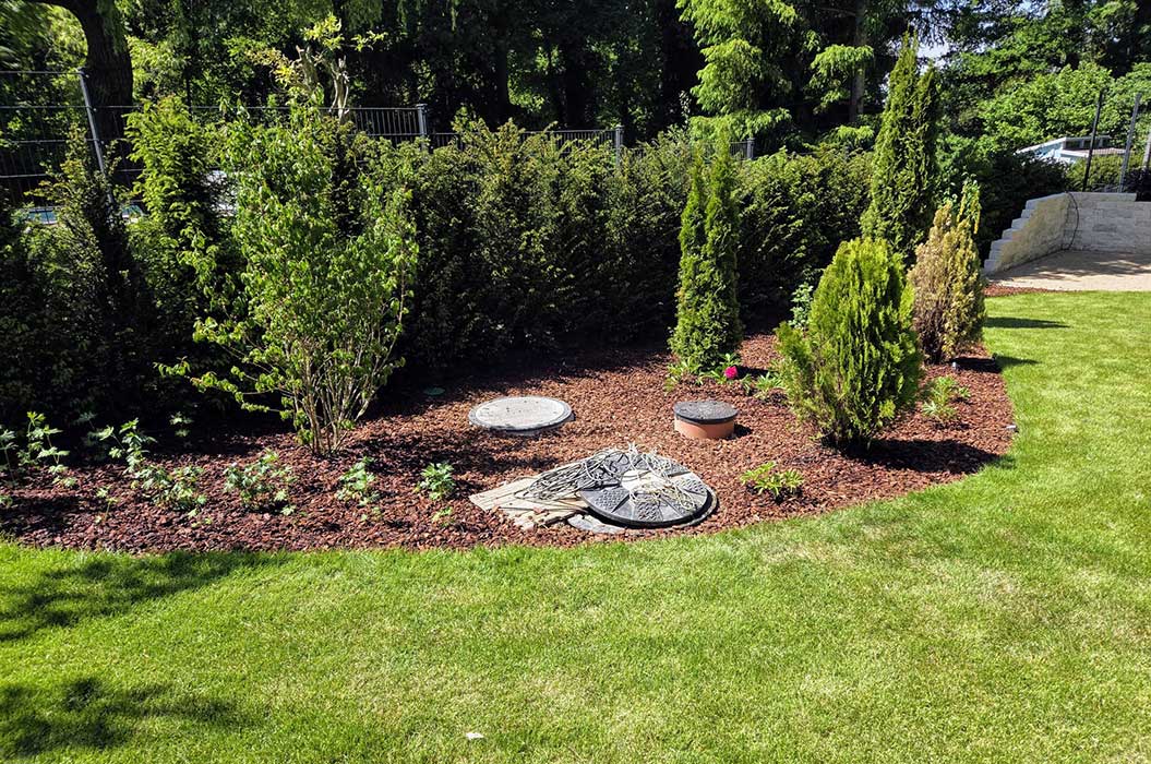 Ein gepflegter Garten mit Rasen und bepflanztem Beet voller Sträucher und Bäume.
