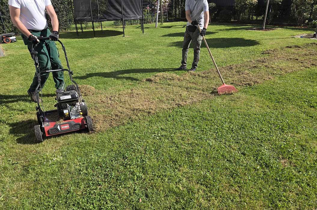 Zwei Personen arbeiten mit einem Rasenmäher und Rechen im grünen Garten.