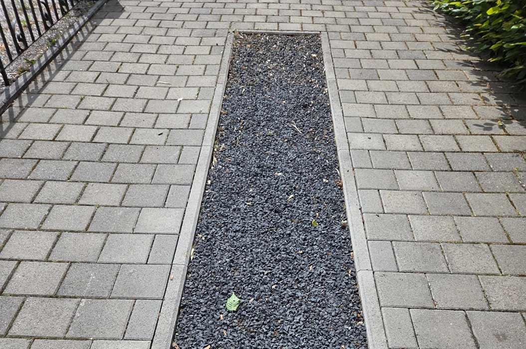 Ein Weg aus grauen Pflastersteinen mit einem schwarzen Kiesstreifen in der Mitte.